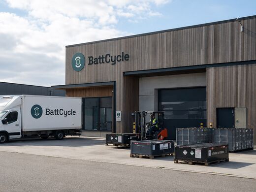 Gebäude mit geparkten Fahrzeugen und Transportbehältern für Batterien im Vordergrund
